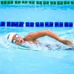 A swimmer energetically performs a freestyle stroke in a clear outdoor swimming pool, showcasing competitive spirit.